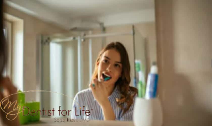 Woman brushing her teeth in a bathroom mirror at a dental practice in Plantation, FL.
