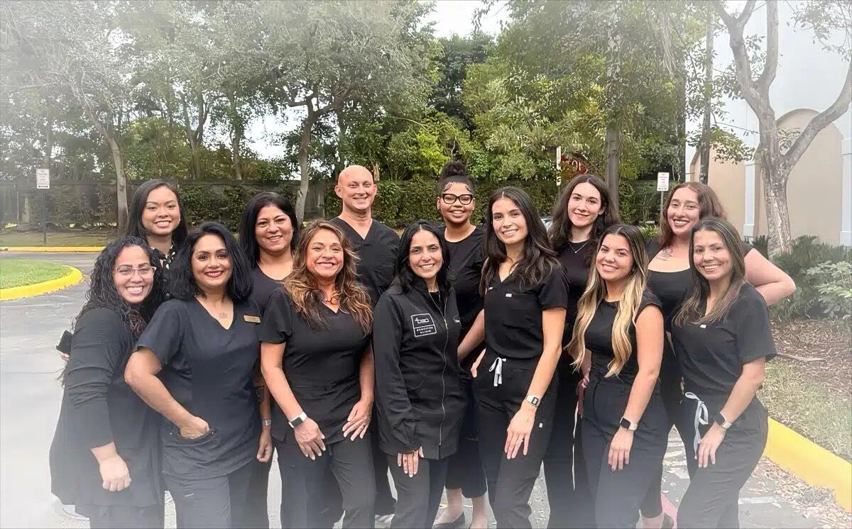 Dental team in black uniforms posing together outside Plantation dental practice location.