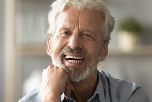 Smiling older man with white hair and beard in dental office setting.