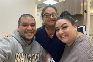 Three dental team members smiling together in a modern dental office setting.