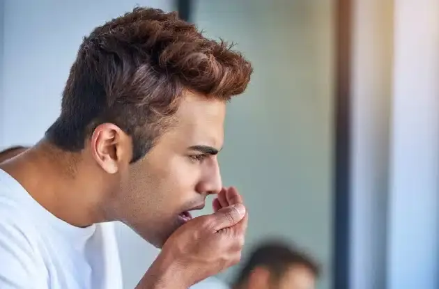 Man experiencing bad breath concerns, covering his mouth with his hand.