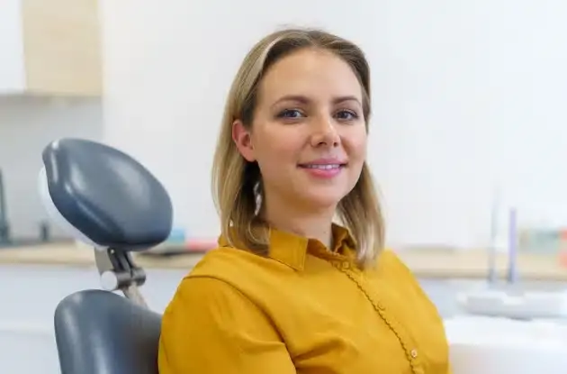 Woman in yellow shirt smiling in dental office treatment room setting.
