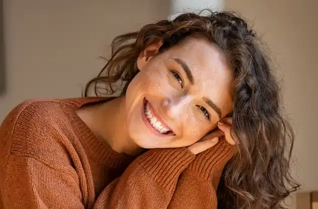 Smiling woman in rust-colored sweater representing holistic dental care in Plantation, FL.