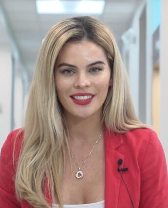 Professional woman smiling in dental office hallway wearing red blazer and microphone.