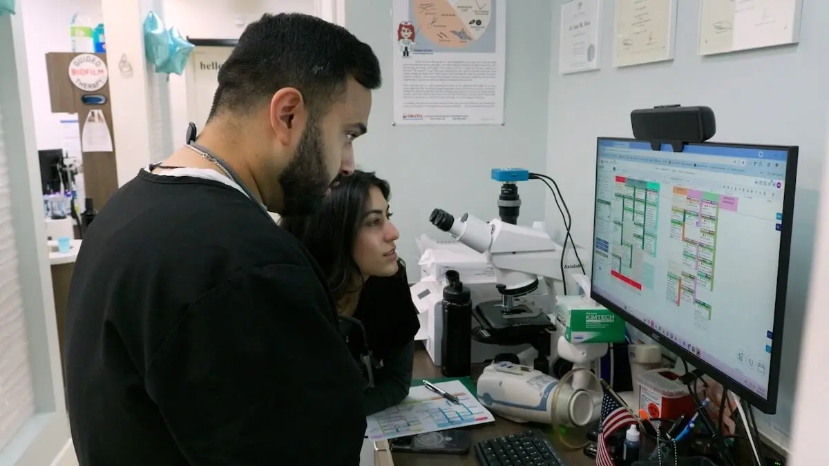Two dental professionals review saliva testing results on a computer screen in a clinical laboratory setting.