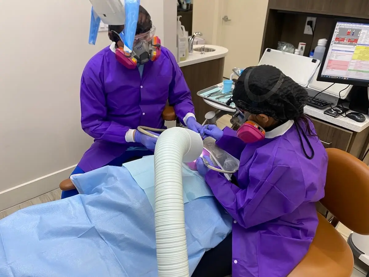 Two dental professionals in purple protective gear performing safe mercury removal procedure.