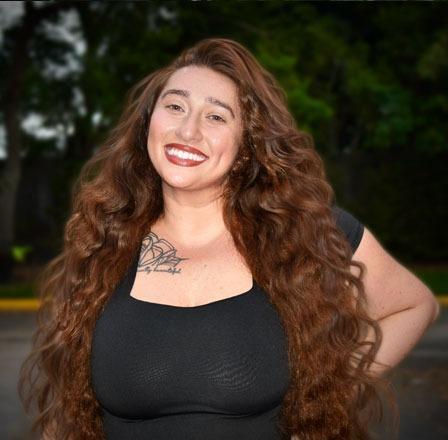 Smiling woman with long wavy brown hair and red lipstick at Plantation dental practice.