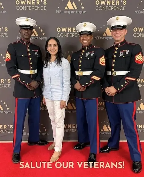 Four Marines in dress uniforms pose with a woman at a veterans appreciation event.