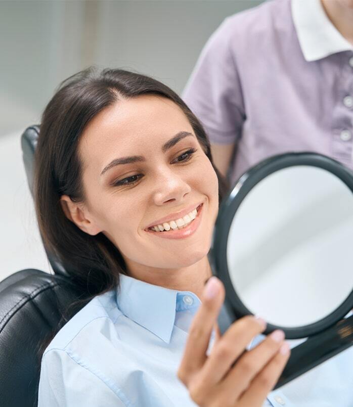 Patient smiling while viewing results in mirror after cosmetic dental treatment at Plantation dental practice.