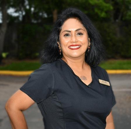 Madhu, dental professional at Plantation, FL practice, smiling outdoors in scrubs.