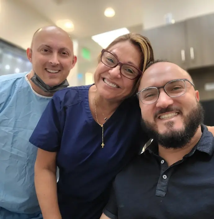Three smiling dental team members posing together in a modern orthodontics office in Plantation, FL.