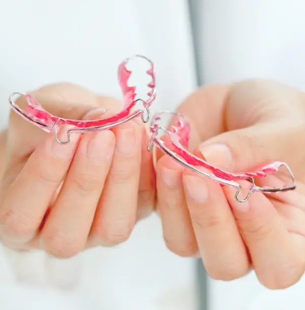 Close-up of pink dental retainers held in hands showing clear orthodontic appliances.